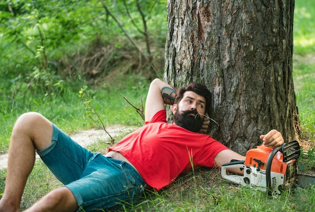 Resting after hard work lumberjack worker with chainsaw in the forest man doing mans job logging har