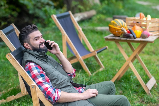 Resting. A man in plaid shirt and vest sitting in the yard