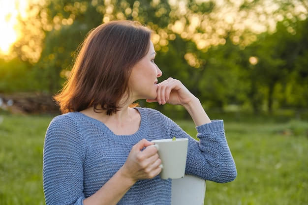 Resting mature woman with cup of tea, female in nature, rustic country style, spring summer day sunset