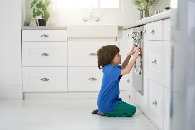 Restless little hispanic boy watching cake baking in the oven, crouching down in the kitchen. Children, cooking concept. Side view