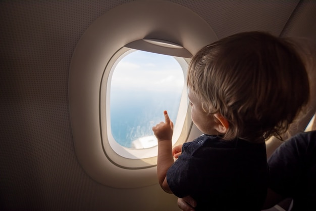 resumption of flights, opening of borders concept. a small child looks at the ocean from the window of a flying plane. first flight. vacation happiness. soft focus