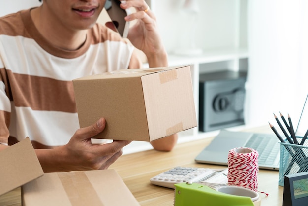 Foto rivenditore in possesso di un pacco postale mentre parla con il suo cliente sul telefono cellulare