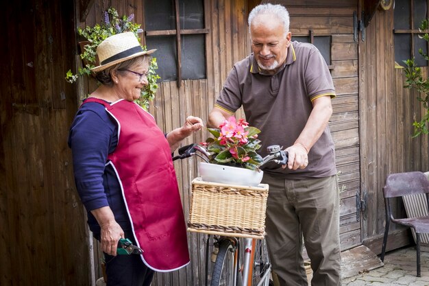 retired adult caucasian couple stay in the garden at his own home to work on the plants and vegetables. old style bike with them