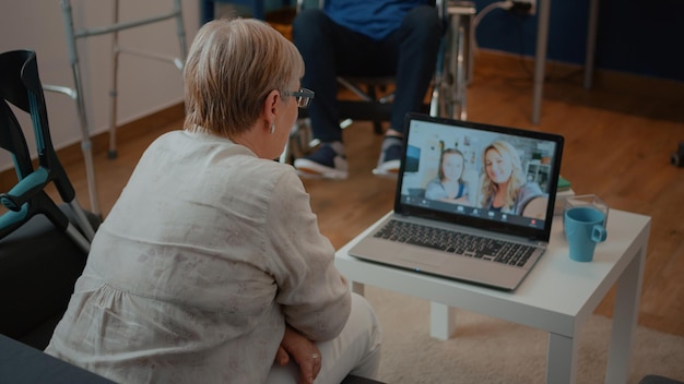 Retired adult talking to family on online teleconference, using\
laptop in living room. retired woman calling daughter and little\
girl on remote videoconference call on internet connection.