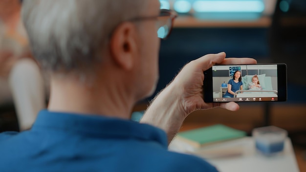 Retired adult using online video call on mobile phone, talking\
to relatives in hospital. older man holding smartphone with video\
teleconference for remote communication with family.