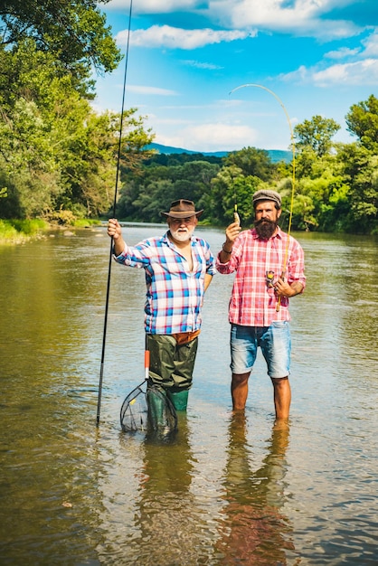 Retired dad and mature bearded son happy bearded fishers in\
water men relaxing nature background brutal man stand in river\
water active sunny day men bearded fishermen