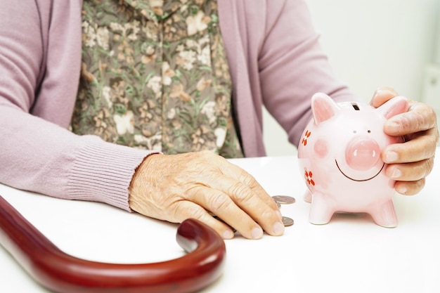 Retired elderly woman counting coins money with piggy bank and worry about monthly expenses and treatment fee payment