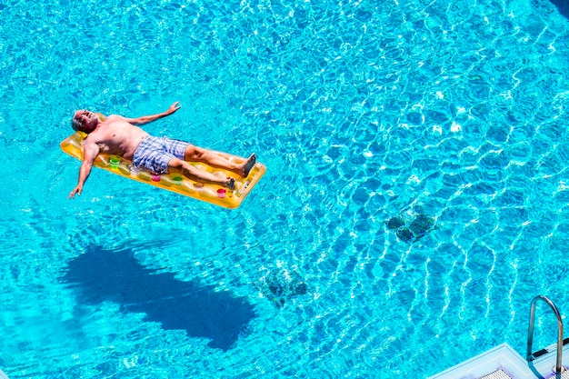 夏休みにオレンジ色のトレンディなリロで眠っている青い水プールをリラックスして楽しんでいる引退したライフスタイルの美しい男シニア年齢