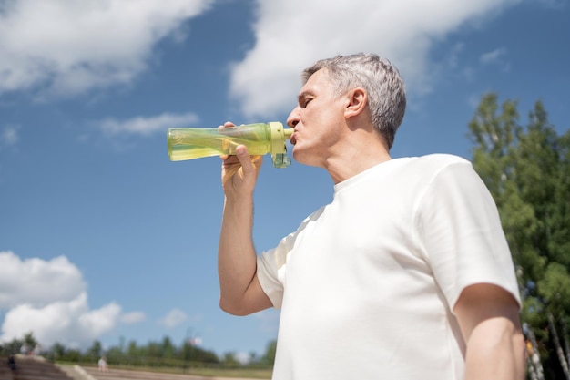 A retired man drinks water from a bottle sports fitness does a workout in the park