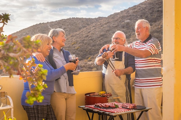 Retired men and women celebrate together in a barbeque cooking activity Mature people and outdoor leisure activity at home Holiday vacation and happy old people talking and smiling together