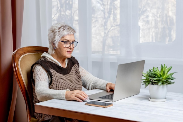 70代の女性がネットで働きながら家でラップトップに座っている