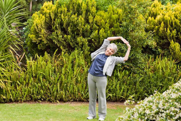 Пенсионер женщина делает ее растяжки в саду