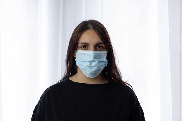 Foto retrato de una chica preocupada con mascarilla en el salon de casa