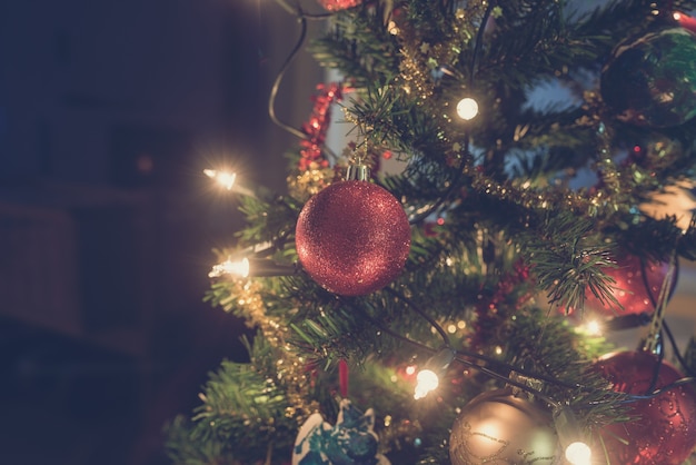 Retro afbeelding van glanzende rode Kerstbal opknoping op versierde vakantieboom met verlichting.