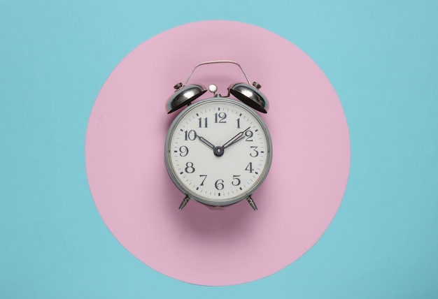 Retro alarm clock on blue background with pink pastel circle. top view