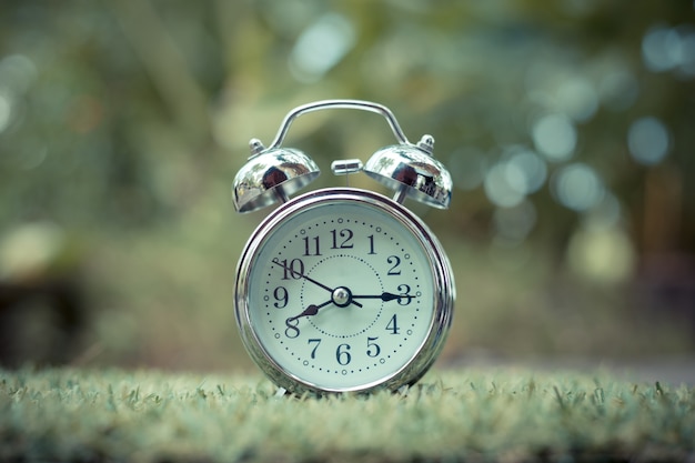 Retro alarm clock on green grass. time concept