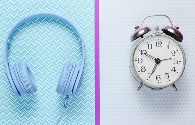 Retro alarm clock and headphones on creative background.