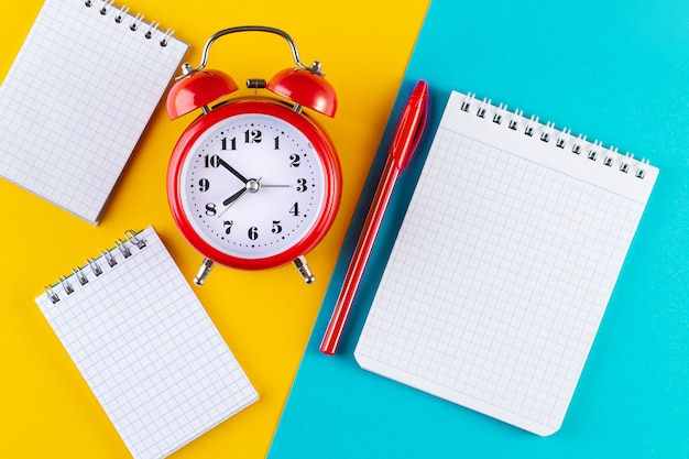 Retro alarm clock next to a pen and notebook on a blue and yellow background.