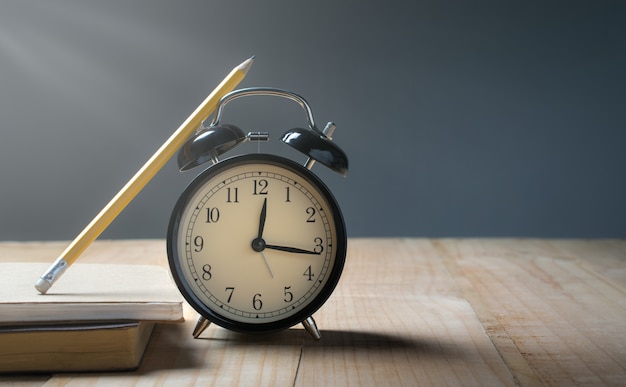 レトロな目覚まし時計、ランチの概念のためのグランジ背景時間と木製のテーブルの上の鉛筆。