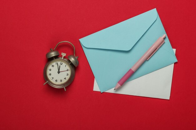 レトロな目覚まし時計、赤い背景の上のサンタの手紙の封筒。午前11時55分。新年、クリスマスのコンセプト。上面図