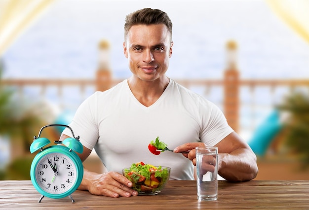 Photo retro alarm clock in which man make intermittent fasting with a healthy food of salad.