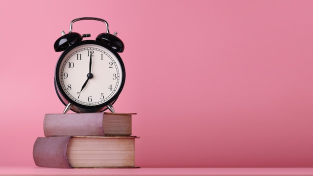 Retro alarm clock with vintage books on pink wooden desk