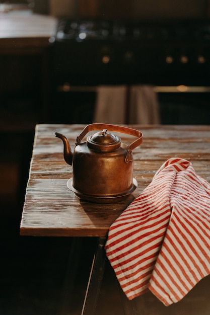 Retro aluminium waterkoker op houten tafel met rood gestreepte handdoek in de buurt. Koperen oude theepot gebruikt voor het maken van thee. Ouderwets keukengerei