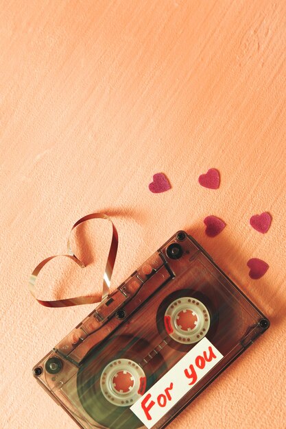 Photo retro audio cassette with tape in shape of heart on pink textured background