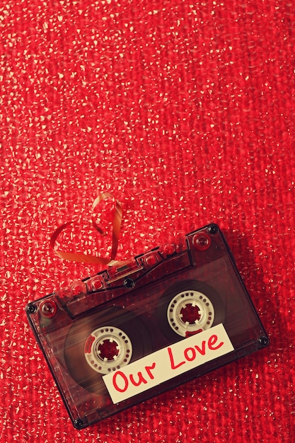 Retro audio cassette with tape in shape of heart on red textured surface