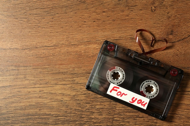 Retro audio cassette with tape in shape of heart on wooden background