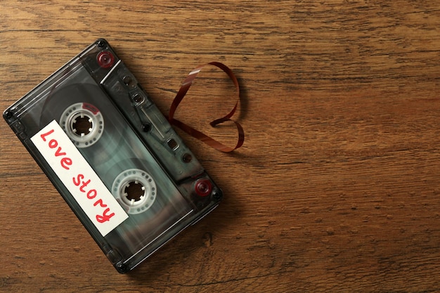 Retro audio cassette with tape in shape of heart on wooden background