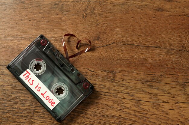 Retro audio cassette with tape in shape of heart on wooden background