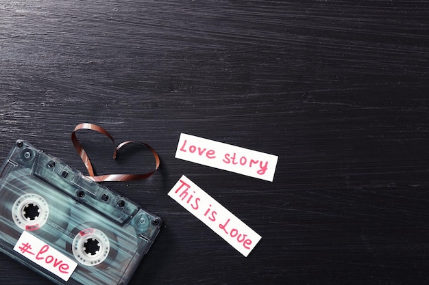 Retro audio cassette with tape in shape of heart on wooden background