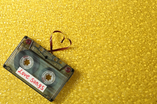 Photo retro audio cassette with tape in shape of heart on yellow textured background