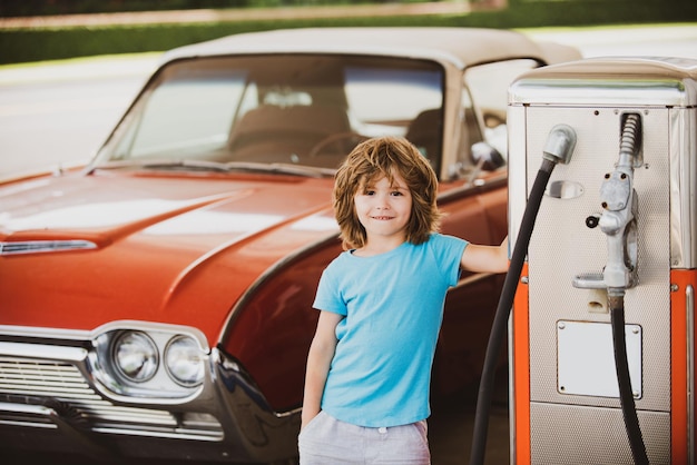 Retro benzinestation. Lachende Kid jongen bij het benzinestation. Wachten op brandstof. Kid tanken vintage auto bij tankstation. Tanken tanken met benzine benzine.