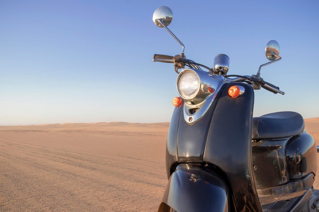 The Retro black scooter at sunset in the golden sand of the Namib Desert