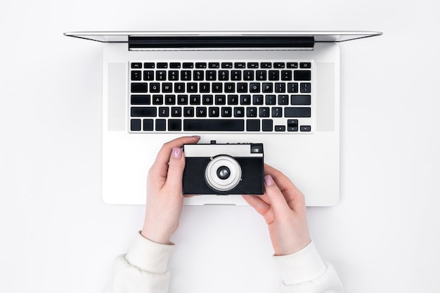 Retro camera in vrouwelijke handen en een laptop op een witte achtergrond bovenaanzicht