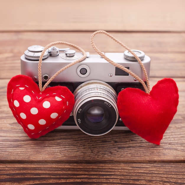 Photo retro camera with red hearts on a wooden background.