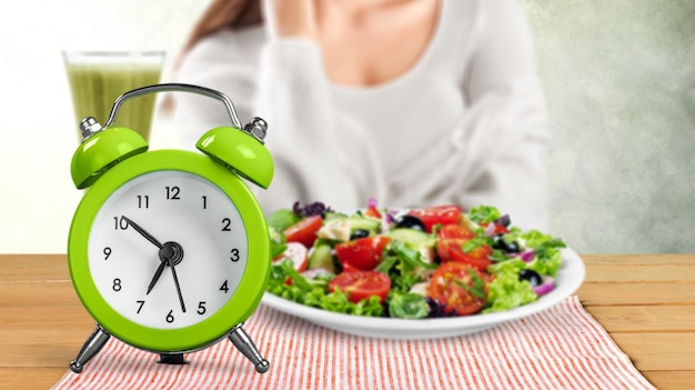 Foto orologio retrò in cui la donna fa il digiuno intermittente con un cibo sano di insalata.