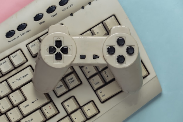 Retro entertainment, gaming. old-fashioned pc keyboard and\
gamepad on blue pink