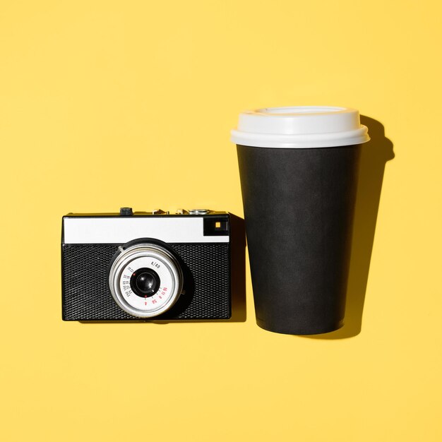 Retro film camera and disposable cup of coffee closeup yellow background flat lay