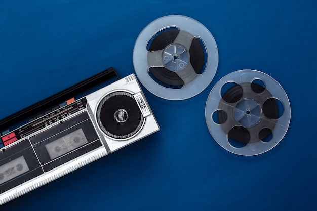 Retro flat lay. retro portable stereo cassette recorder and\
audio magnetic tape reel on classic blue