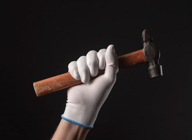 Photo retro hammer tool in male hand in white building gloves close up over black background.