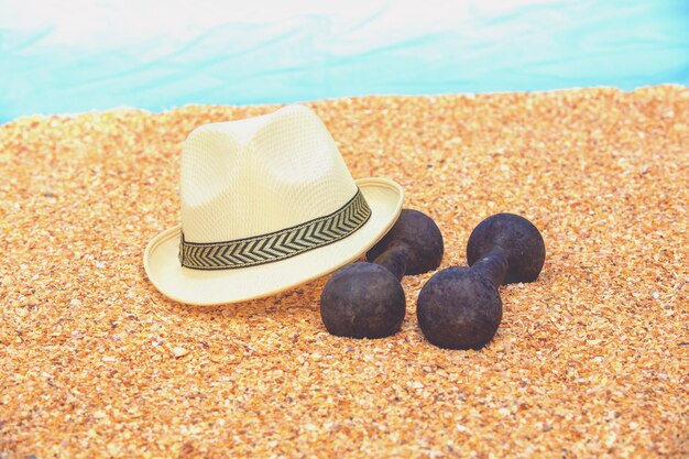 Retro iron dumbbells and male hat on the beach