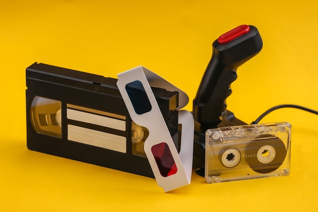 Photo retro joystick with 3d glasses, audio and video cassette on yellow background. attributes 80s