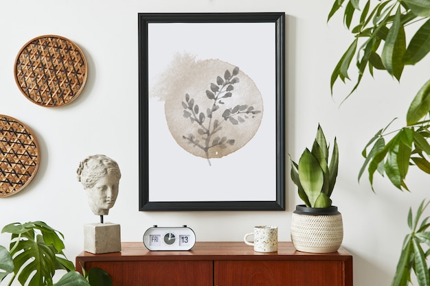 Retro modern compositon of living room interior with design teak commode, black frame, clock, plant, decoration, white wall and personal accessories..