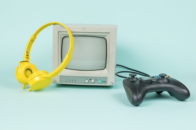 Retro monitor, gele koptelefoon en een gameconsole op een blauwe achtergrond. Vintage apparatuur.