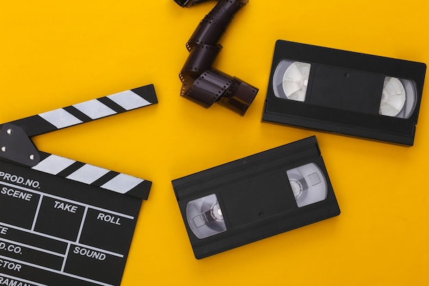 Retro Movie clapper board,  video cassette and film tape on yellow background. Filmmaking, Movie production. 80s. Top view