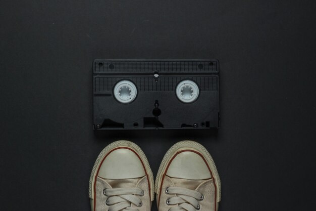 Retro old sneakers and video cassette on black background. 80s. Top view