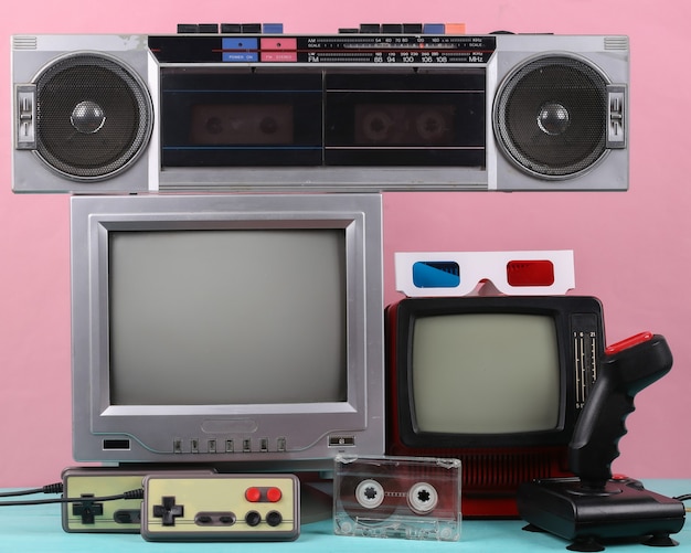 Mini televisori portatili retrò, giradischi, joystick, gamepad, audiocassetta su sfondo rosa. attributi anni '80, media retrò, intrattenimento